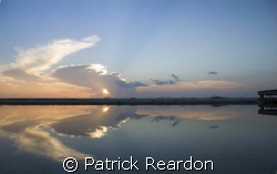 The sunset is reflected in the calm waters of an inlet on... by Patrick Reardon 